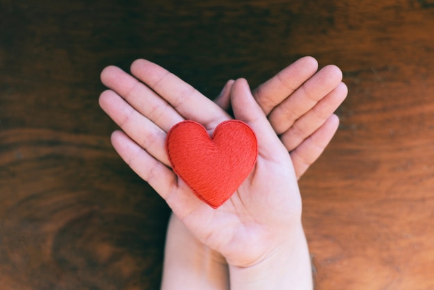 Cuore in mano per il concetto di filantropia - donna con cuore rosso sulle mani per San Valentino o donare aiuto dare amore calore prendersi cura di sfondo in legno