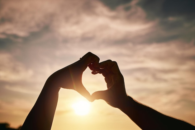 Cuore mani tramonto sulla spiaggia e silhouette con segno amore e romanticismo persone viaggiano e all'aperto Avventura emoji e cura con la salute nella natura supporto e impegno coppia con fiducia e mare