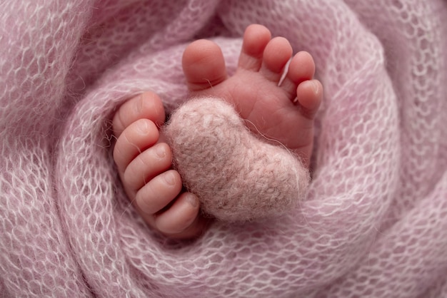 Cuore rosa lavorato a maglia nelle gambe di un bambino Piedi morbidi di un neonato in una coperta di lana rosa Primo piano delle dita dei piedi, talloni e piedi di un neonato Macrofotografia il piedino di un neonato