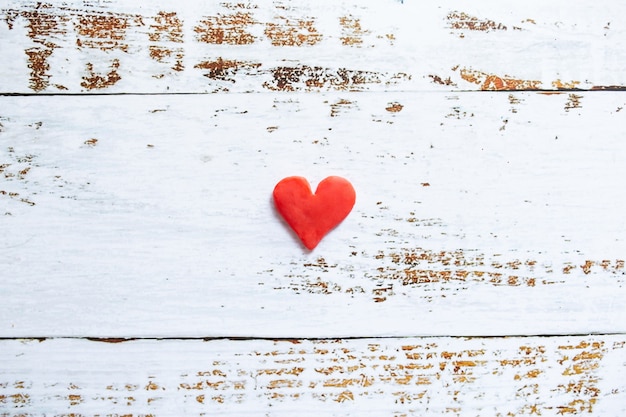 Cuore rosso di plastilina su fondo di legno bianco.