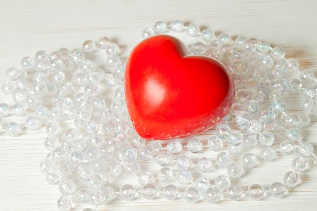 Cuore rosso di San Valentino con perle di vetro su una superficie di legno bianca con perle di vetro. disteso, spazio per il testo.