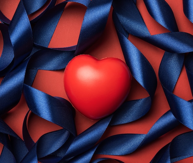 Cuore rosso e nastro arricciato di seta blu su sfondo rosso, giorno di San Valentino, vista dall'alto