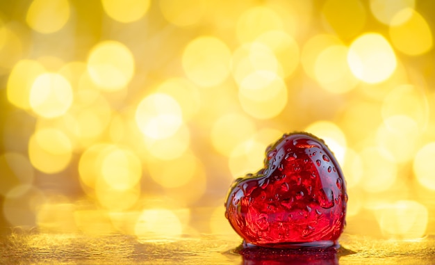 Cuore rosso trasparente in gocce d'acqua su uno sfondo dorato con bokeh. sfondo d'amore. San Valentino