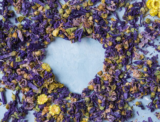 Cuore sciolto di erbe aromatiche della lavanda e della camomilla del tè asciutto sulla macro di legno blu della tavola