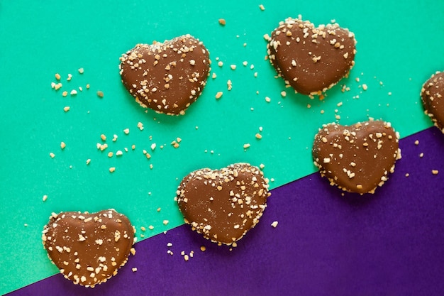 Cuori di biscotti al cioccolato con noci su sfondo colorato piatto su scaglie di cioccolato di carta colorata