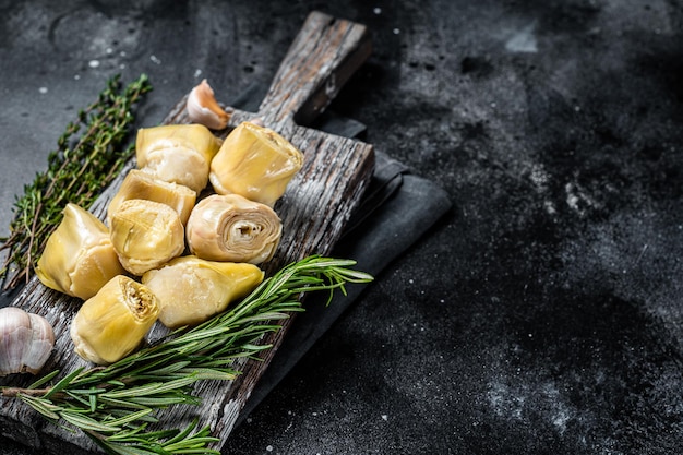 Cuori di carciofi marinati con olio d'oliva ed erbe aromatiche carciofi marinati con aglio su tavola di legno Sfondo nero Vista dall'alto Spazio copia
