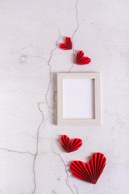 Cuori di carta fai da te rossi attorno a una cornice fotografica vuota su una vista verticale concreta di San Valentino