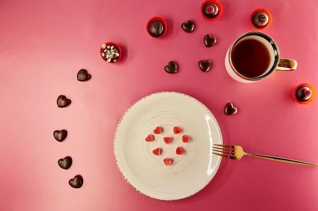 Cuori di ghiaccio su piatto d'epoca bianco con forchetta Cuori di cioccolato e dolci decorati Sfondo sfumato rosa Cena romantica creativa Concetto di San Valentino Vista dall'alto