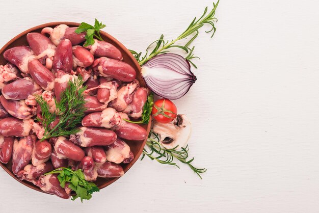 Cuori di pollo crudi sul piatto pronti per la cottura con rosmarino e spezie su uno sfondo di legno bianco Vista dall'alto Spazio libero per il testo