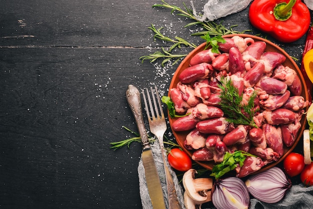 Cuori di pollo crudi sul piatto pronti per la cottura con rosmarino e spezie su uno sfondo di legno nero Vista dall'alto Spazio libero per il testo