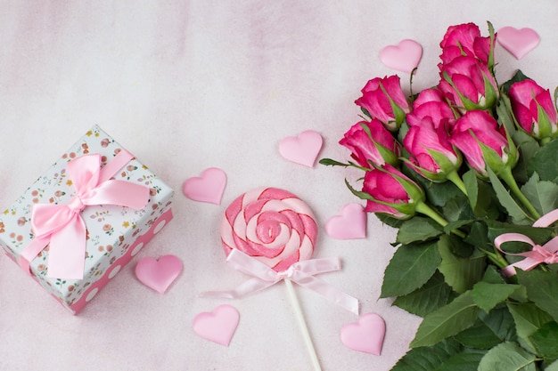 cuori di raso rosa, caramelle, un mazzo di rose rosa e un regalo in una scatola