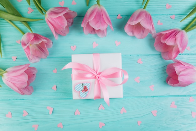 Cuori rosa dei tulipani, del regalo e della carta su fondo di legno blu