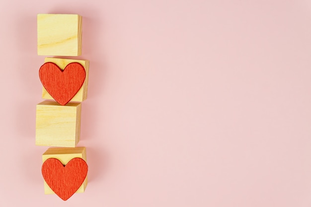 Cuori rossi e cubi di legno su sfondo rosa. Piatto creativo laici con lo spazio della copia. Biglietto di auguri festivo per San Valentino.