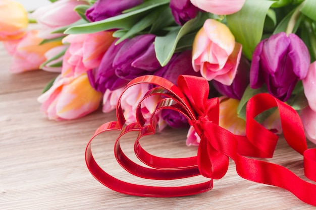 Cuori rossi e fiocco con tulipani rosa e viola sullo sfondo