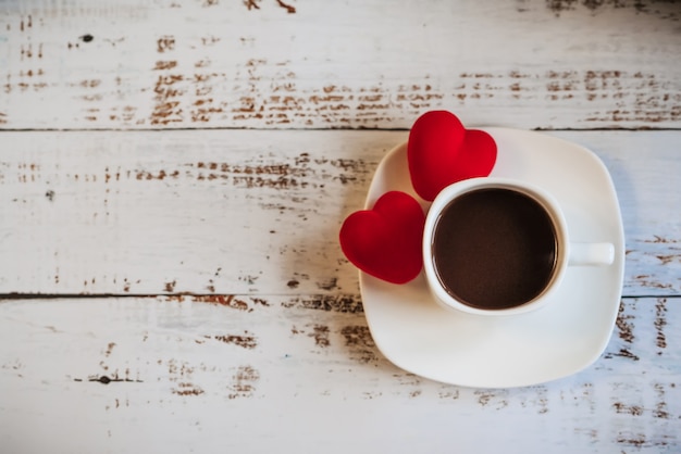 Cuori rossi e una tazza di caffè su un fondo di legno bianco