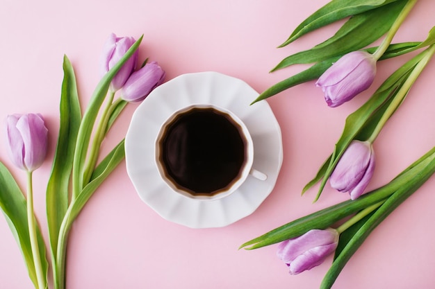 Cup of coffee and purple tulips on pink background flat lay top view flower composition spring time