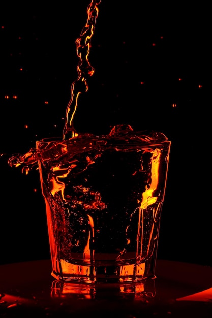 Cupa natura morta con un bicchiere. L'acqua arancione viene versata in un bicchiere da whisky