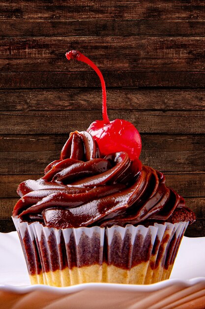 Cupcake al cioccolato con ciliegia su un piatto sul tavolo di legno.