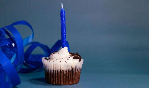 cupcake al cioccolato con una candela blu, sfondo blu e nastro blu