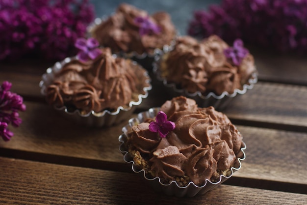 Cupcake alla vaniglia fatto in casa con glassa di cioccolato su fondo di legno in legno con messa a fuoco selettiva lilla. Delizioso dessert per il compleanno, le festività natalizie, il fidanzamento o il giorno di San Valentino