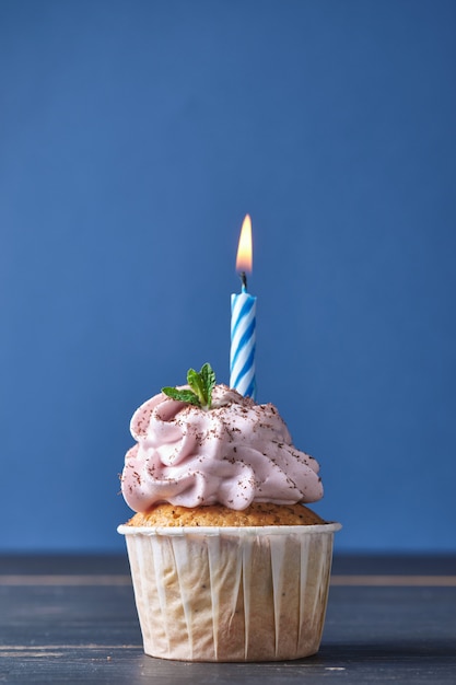 Cupcake celebrativo con una candela. Il cupcake è decorato con crema rosa, foglie di menta e gocce di cioccolato.