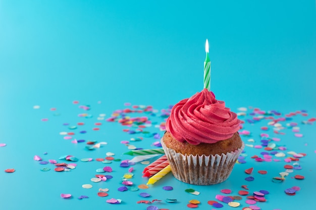Cupcake compleanno rosa con candela verde e coriandoli su sfondo blu