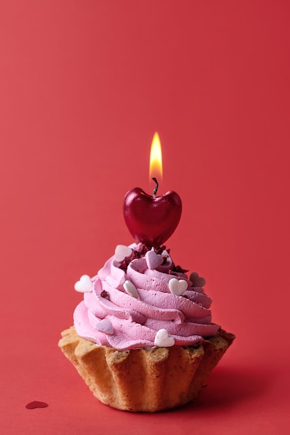 Cupcake con crema e candela a forma di cuore che brucia su sfondo rosso, San Valentino, simbolo d'amore.