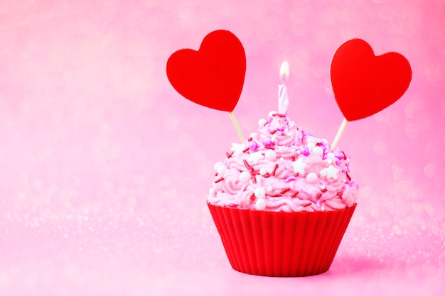 Cupcake con crema rosa, cuore rosso e sparkler su sfondo rosa. Cibo per San Valentino.