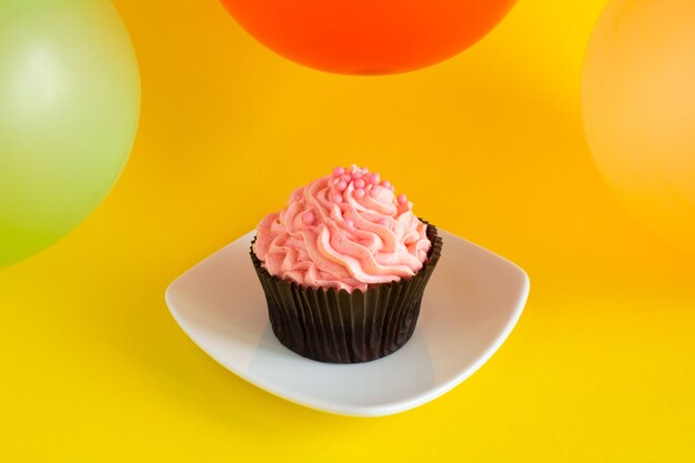 Cupcake con crema rosa e palloncini colorati su sfondo giallo