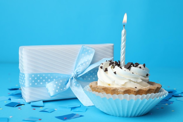 Cupcake di compleanno con candela e scatola regalo su sfondo blu chiaro