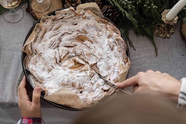 Cupcake di Natale Una mano femminile taglia una torta di mele fatta in casa di Natale cosparsa di zucchero a velo bianco torte fatte in casa su una vista dall'alto del tavolo di Capodanno decorato festivo Concetto di cucina festiva