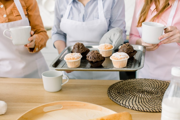 Cupcake, muffin, cottura insieme - tre donne tengono cupcakes al cioccolato e vaniglia appena sfornati sulla teglia. Cucina familiare, concetto di festa della mamma