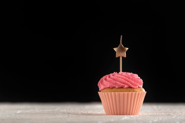 Cupcake rosa con candele a forma di stella su sfondo nero. Copia spazio. Tortini di festa.