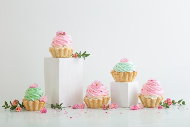 cupcake rosa e verdi con fiori di primavera su podi di legno su sfondo bianco