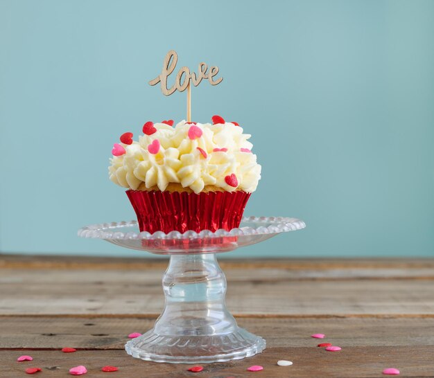 Cupcake su un espositore con crema e decorazione di topping rosso su uno sfondo di legno con un segno