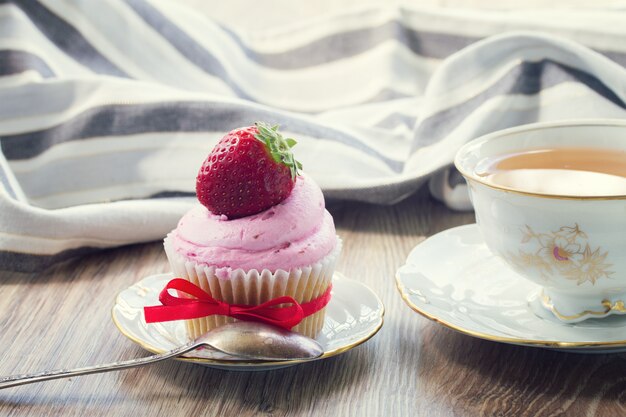 Cupcake vintage con fragole fresche nel piatto e tazza di tè sulla tavola di legno