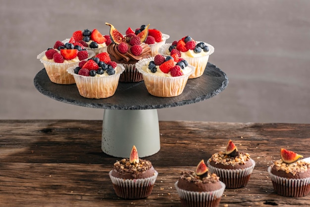 Cupcakes al cioccolato e vaniglia con mix di frutti di bosco sul supporto sul tavolo Muffin con frutti di bosco su sfondo grigio