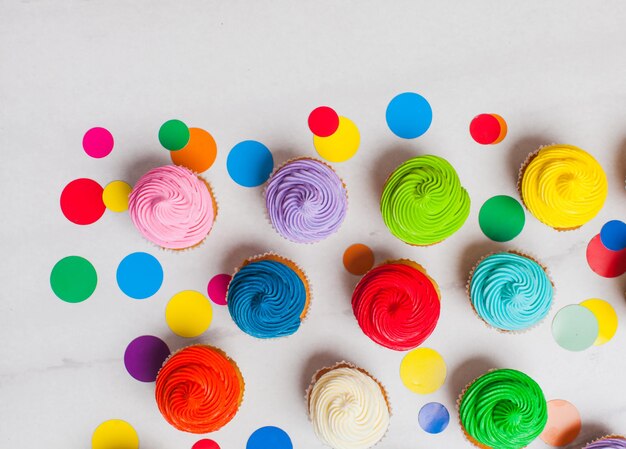 Cupcakes colorati piatti giacciono sullo sfondo di marmo con spazio per la copia. Stile pop art con coriandoli di cerchi arcobaleno
