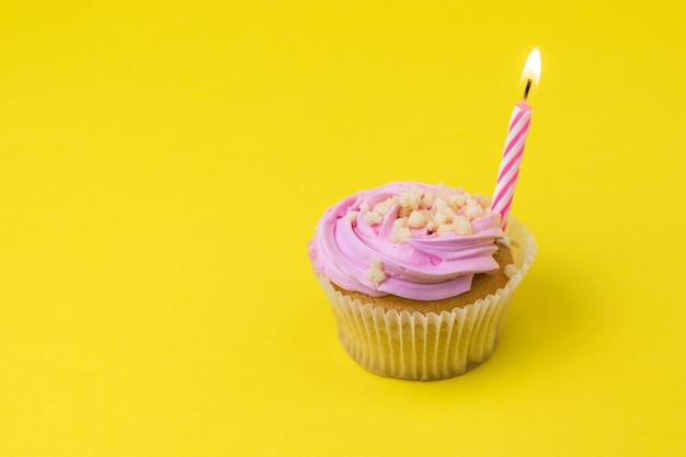 Cupcakes con crema ai frutti di bosco e una candela su una superficie gialla