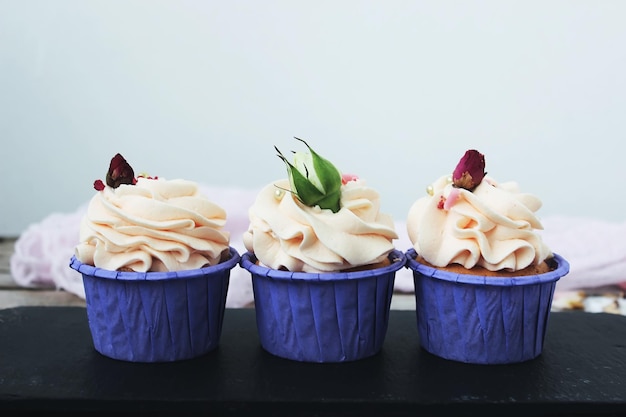 Cupcakes con crema delicata in un supporto lilla, decorato con fiori su un tavolo bianco. Messa a fuoco selettiva.