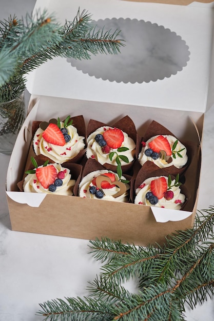Cupcakes con crema di formaggio cremoso e ripieno di frutti di bosco Dolci per le feste Dessert decorato con frutti di bosco freschi foglie verdi confezionati in scatola regalo