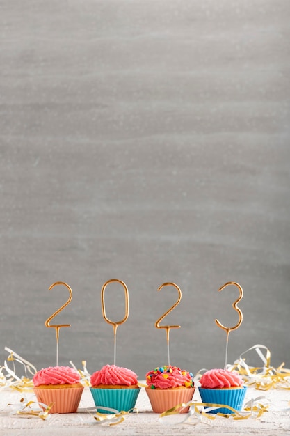Cupcakes di Capodanno e stelle filanti d'oro numeri 2023 muffin per le vacanze con glassa di crema al burro rosa Sfondo grigio Spazio di copia