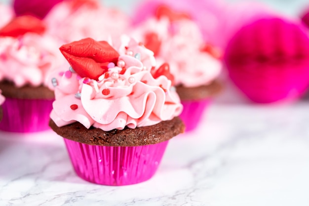 Cupcakes di velluto rosso con glassa di crema al burro rosa italiana e decori con cioccolatini rossi a forma di cuore e bacio.