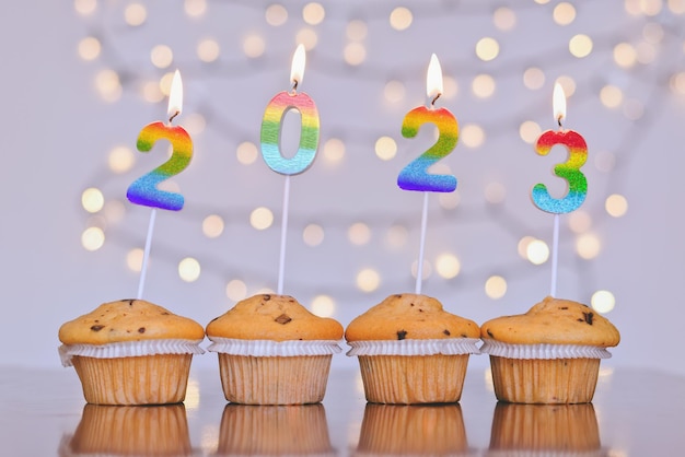Cupcakes dolci di Natale e candele accese a forma di numeri 2023. Sfondo bianco con bokeh.