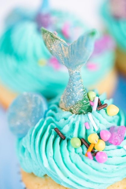 Cupcakes gourmet a forma di sirena conditi con glassa di crema al burro blu e decorati con confettini e code di sirena al cioccolato.