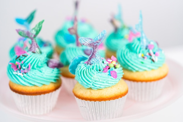 Cupcakes gourmet a forma di sirena conditi con glassa di crema al burro blu e decorati con confettini e code di sirena al cioccolato.