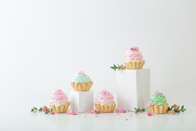 Cupcakes rosa e verdi con fiori di primavera su podi in legno su sfondo bianco