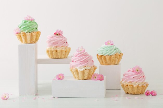 Cupcakes rosa e verdi con fiori di primavera su podi in legno su sfondo bianco