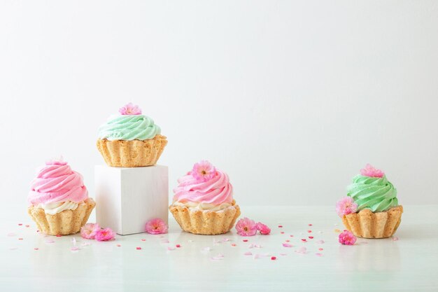 Cupcakes rosa e verdi con fiori di primavera su podi in legno su sfondo bianco