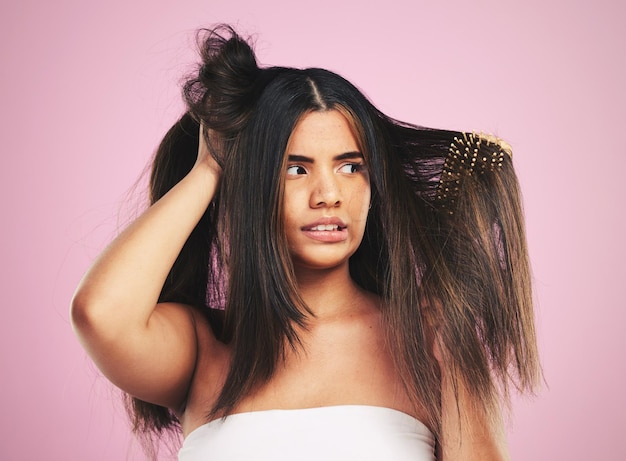 Cura dei capelli e studio di donna con groviglio di spazzole e stress con viso frustrato su sfondo rosa Modello di ragazza e ansia per errore fallito e pensiero con pulizia di bellezza e crisi cosmetica